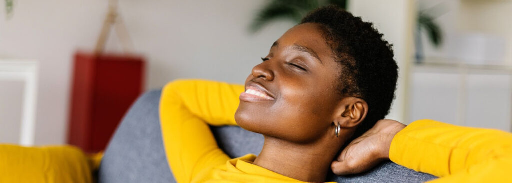 An adult lady is comfortably relaxed on a couch with a smile on her lips after she successfully paid off her loans early