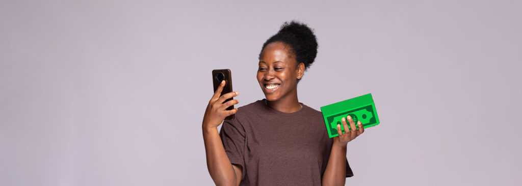 A lady staring at her phone and holding a wad of cash with excitement after repaying her loans on time