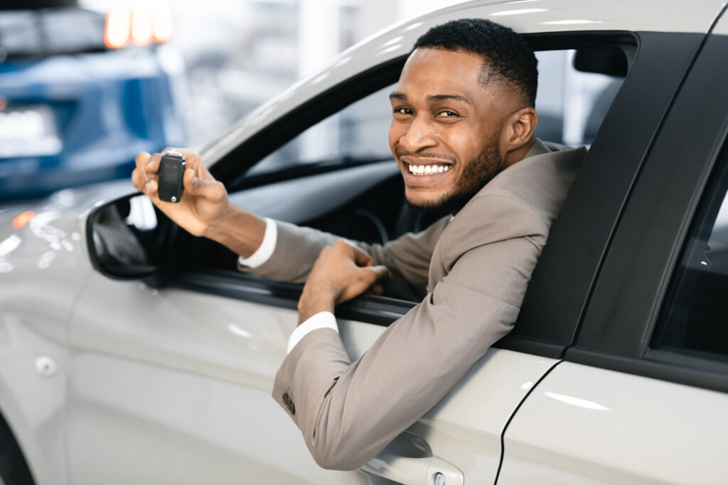 A young man is peeping out his car door and dangling car keys he got through a personal loan