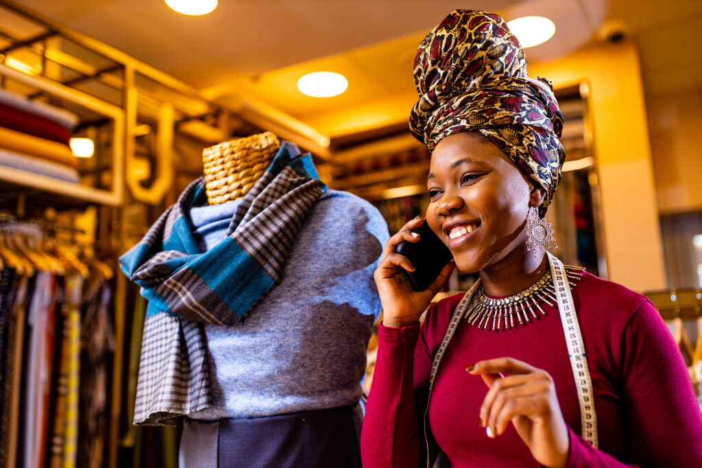 A tailor who understands why loans are good and important is at her visibly thriving shop with a phone to her hear